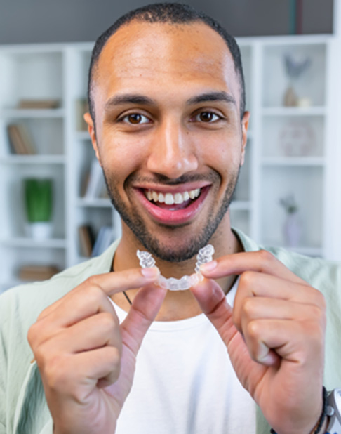 Man holding an Invisalign aligner and smiling