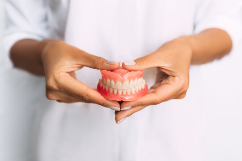 Woman holding full set of dentures with two hands in front of her white clothing